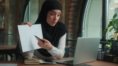 Müslüman Arap İslami kız tesettürlü gülümseyen kadın iş kadını kadın dizüstü bilgisayar video görüşmeleri kağıt dökümanına işaret ederek online çatışma rapor satış grafiği iş sunumunu tartıştı