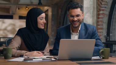 İki iş arkadaşı ofis kafesinde şirket işlerini tartışıyor. Çok ırklı erkek çalışanlar, Hintli erkek Müslüman kadın tesettürlü çeşitli iş kadınları dizüstü bilgisayarlar yazıyor.