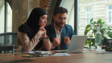 İki çok ırklı iş ortağı erkek işçi erkek Müslüman kadın masadaki tesettüre katılmış Hint iş kadını dizüstü bilgisayar ekranına bakıyor.