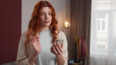 Neşeli Kafkasyalı kadın cep telefonu görüntüsü veriyor. Evde ekranı kaydırıyor. Olumlu duygulardan tatmin olan kadın gülümsemesi. İnternetteki video kayan web kızı sanal oyun oynarken sohbet ediyor.