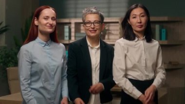 Üç kendine güvenen çok ırklı kadın iş yeri beyaz Asyalı meslektaşları kameraya bakıp gülümsüyor. Çok ırklı pozlar veriyor, el ele tutuşuyor, iş arkadaşları iş arkadaşları çeşitliliği gösteriyor.