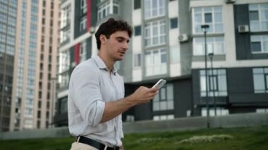 Kafkasyalı bir adam cep telefonu işini açık havada geziyor internet bağlantıları kuruyor uygulamalı erkek işadamı sohbet ediyor akıllı telefon, internet, sosyal medya işvereni profesyonel cihaz yürüyüşü