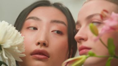 İki farklı etnik çeşitliliğe sahip kadın, Çinli Asyalı genç kızlarla karşı karşıya. Japon Koreli Çinli kadınlar temiz cilt doğal organik kozmetik cilt bakım şampuanı kapalı alanda çiçek parfümü tutuyorlar.