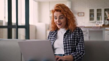 Gülümseyen mutlu kullanıcı kadın sanal kazancı kutluyor. Şaşırtıcı sohbet dizüstü bilgisayarı okuyor. İyi haberler okuyor. Kanepede oturan beyaz kadın internette sohbet ediyor.