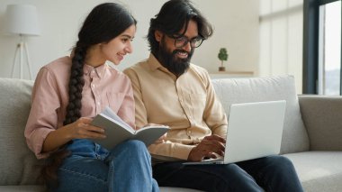 Dizüstü bilgisayarlı çift ev bütçesi planlayan ev kredisi ödemelerini ödemeli Arap kadın karısı not defterinde Hintli adam kocası evdeki bilgisayar aile işleriyle ilgili veri e-postaları yazıyor.
