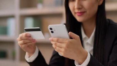 Gülümseyen mutlu Asyalı iş kadını Koreli Çinli işkadını ofis çalışanı cep telefonu akıllı telefon kullanıcısı kredi kartı yazıcı şifreli ev içi satın alma