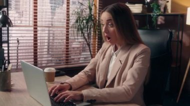 Şaşırtıcı bir şekilde Kafkasyalı iş kadını kadın ofis çalışanı serbest çalışan iş kadını dizüstü bilgisayarda çalışan iş kadını kameraya bakıp haykırarak zafer kazandı.