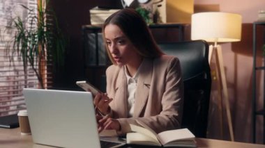 Endişeli Kafkasyalı iş kadını kız iş kadını ofis çalışanı serbest girişimci cep telefonu görüşmesi planlama randevusu notları yazma ev bilgisayarında çalışma