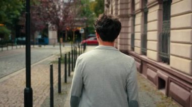 Tanımlanamayan bir adamın arkasından arka manzara. Şehre doğru yürüyen, gülümseyen, kameraya bakan bir adam. Sen gülümseyen, dişlek, turist portresi.