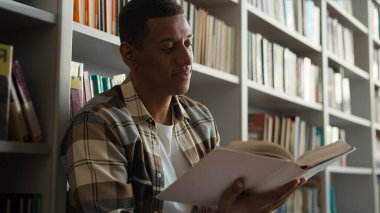 Afrikalı Amerikalı bir adam kütüphanede oturmuş kitap okuyordu. Zevk hobileri okuyordu. Hikaye öğreniyordu.