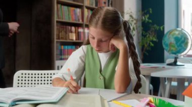 Kafkas öğretmenliği profesörü kadın öğretmen öğrenci görevini kontrol ediyor. Hatayı düzeltiyor. Küçük kız çocuğuna yardım ediyor.