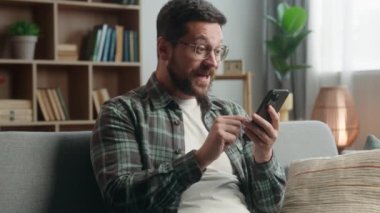 Neşeli, neşeli, mutlu, mutlu, mutlu, bağrışan, mutlu adam, cep telefonu kullanan, erkek oyuncu, sevinç çığlıkları atan, video oyunu kazanan, zafer kazanan akıllı telefon kazanan, ev sahibi koltukta kutlama yapan, mutlu adam.