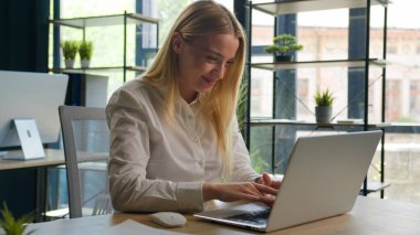 İş projesiyle uğraşan beyaz bir kadın ofisteki dizüstü bilgisayarında e-posta yazıyor mutlu bayan iş kadını yönetici internet bilgisayarlarında geziniyor neşeli kız gülümsemesi üzerine çalışıyor.