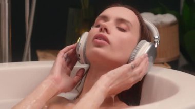Rahatlamış dinlenen sakin sakin beyaz kadın sıcak küvette dinleniyor müzik kulaklıkları dinliyor podcast müzik kulaklıkları banyodaki güzellik spa meditasyonunda bir kadın.