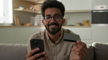 Gülümseyen mutlu Arap erkek müşteri müşteri müşteri müşteri tüketici adam telefon kartı mobil banka uygulaması ile online alışveriş ev mutfağından gıda teslimatı satın almak e-bankacılık hizmeti için ödeme parası