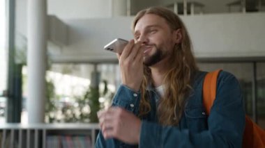 Mutlu kullanıcı kaydı sesli mesaj konuşması akıllı telefon mikrofonuyla konuş üniversite üniversitesinde konuşan ve gülümseyen beyaz erkek öğrenci cep telefonu komutuyla konuş.
