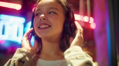 Beyaz, Asyalı, müzik kulaklığı teknolojisi dinleyen bir kız çocuğu. Neon neon kaygısız liseli çocuk dans ediyor. Kablosuz bağlantı cihazı kullanıyor, gülümsüyor.