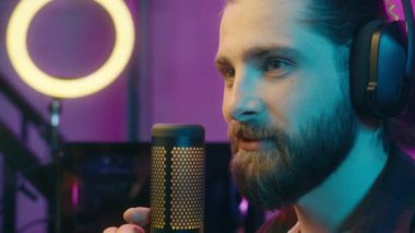 Dertsiz gülümseyen Kafkas erkek adam blogger streamer bağımlısı dokunmatik mikrofon akışı radyo oyuncusunu etkileyen ev sahibi sunucu Neon Akşamında insan siber Spor PC oyun blogu tartışan