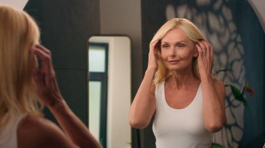 Güzel, beyaz, olgun, yaşlı bir kadın banyoya mutlu, orta yaşlı bir kadın gelir. Makyaj stili güzelliğini ayna yansımasında kontrol eder. Günlük cilt bakımı, yaşlanmayı önleyen doğal kozmetik ürünler.
