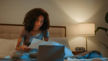 Evde geç saatlere kadar çalışan meşgul Afro-Amerikan kız öğrenci internetten bilgisayarla incelemeye hazırlan. Kadın iş kadını, evrak işleri, yurt içi elektrik faturalarını kontrol et.