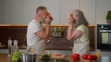 Komik, beyaz, yaşlı, mutlu, aile babası, mutlu, yaşlı bir adam birlikte somurtarak eğleniyor. Kırmızı biber biberleri yapıyor. 50 'li yaşlarda, olgun bir koca, mutfakta sebze pişiriyor.