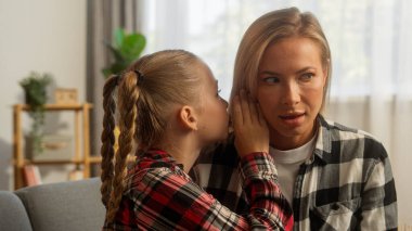 Şok olmuş beyaz kadın anne kadın aile kızı evde küçük kız çocuğunun dedikodularını dinliyor gülümseyen küçük kız öğrenci kız anne kız ile sırrını paylaşıyor dedikoduların komik velayeti hakkında konuşuyor