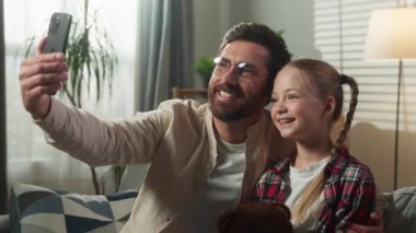 Kafkasyalı mutlu aile cep telefonuyla selfie çekiyor. Gülümsüyor, birlikte poz veriyorlar. Erkek baba maske takıyor.