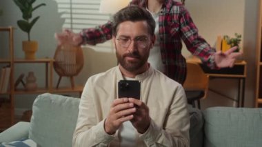 Kafkasyalı erkek kullanıcı evde kanepe babası cep telefonu uygulamasına göz atıyor akıllı telefon, küçük kız, çocuk, aniden sürpriz atlama, baba, gülen aileyi oynuyor.