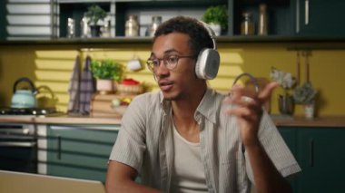 Gülümseyen Afrikalı Amerikalı etnik erkek iş adamı ev mutfağında online video konferansında serbest çalışan bilgisayar konuşmaları kulaklıkla iletişim kurma eğitimi alan.