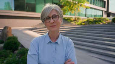 Açık hava portre işi girişimcisi yetişkin 50 'li yaşlarda kadın Kafkas iş kadını olgun orta yaşlı, yaşlı, beyaz saçlı, kendine güvenen kadın şehirde kameraya bakan başarılı bir çapraz el kamerası.