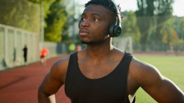 Düşünceli Afrikalı Amerikalı sporcu kulaklıklı sporcu şehirde akıllı adam kullanıyor spor eğitimi için hazırlan erkek koşucu ara verdiğinde dışarıda sabah koşusunda kardiyo egzersizi yap stadyumda