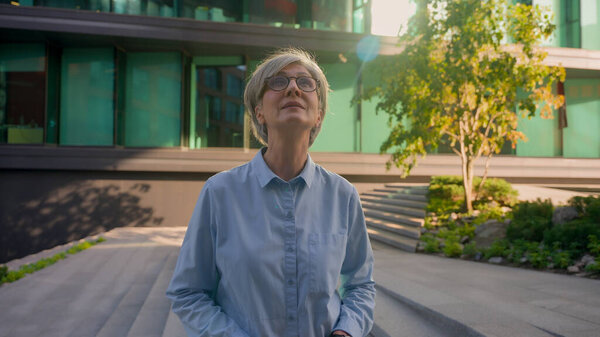 Portrait business lady Caucasian 50s adult mid age gray-haired mature woman senior old female looking around in city center successful inspired elder businesswoman smiling look away dreaming outdoors