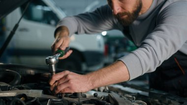 Otomobil istasyonunda çalışan beyaz tenli profesyonel oto tamircisi erkek motor tamircisi garajda anahtarı anahtarla bozuk araba tamir ediyor.