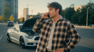 Stresli şoför Kafkasyalı adam konuşuyor. Cep telefonundan araba servisini arıyor. Açık yolda duruyor.