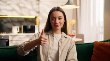 Mutlu, beyaz, bayan bayan bayan bayan, oturma odasında, kanepede otururken gülümsüyor, başparmak hareketi yapıyor, başarılı oluyor, iyi sonuç, yüksek kalite, mükemmel.