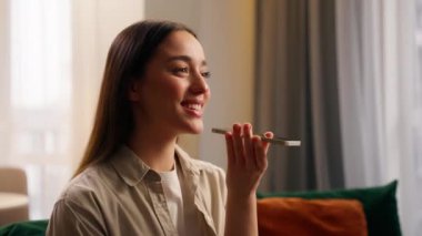 Mutlu akıllı telefon kullanıcısı, beyaz kadın, cep telefonundaki ses dosyasını kaydediyor. Gülümsüyor, sesli mesaj kaydediyor. Ev neşesi iletişim uygulamasında cep telefonuyla konuşarak cevap veriyor.