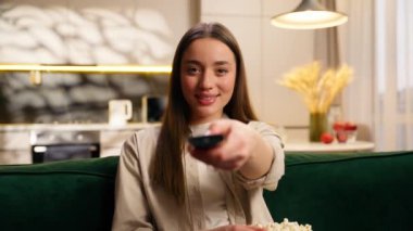 Beyaz kadın bayan bayan kanepede dinleniyor haftasonu kanepede patlamış mısır yiyor uzaktan kumandalı TV film programı seyrediyor ve gülümsüyor.