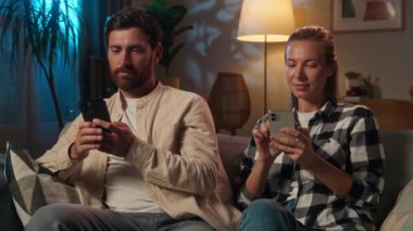 Gadgets bağımlısı çift Kafkas kadın ailesi, akıllı telefonları kullanıyor. Kanepe üzerinde gece evde internet, sosyal medya aşırı kullanım kız bağımlısı koca eş, internet üzerinden cep telefonu alışverişi yapıyor.