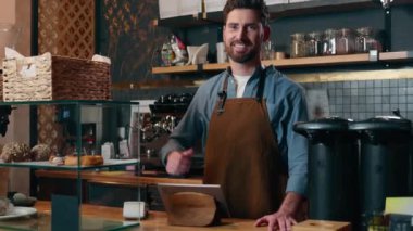 Tatmin olmuş Kafkasyalı barmen adam küçük işletme sahibi kafeterya kafeteryasında el hareketi yapan mutlu garson gülümseyen yetişkin bir erkek garson öneriyor.