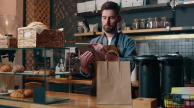 Gülümseyen Kafkasyalı teslimatçı, tablet teknolojisinin sipariş faturasını hesapladı. Kafeteryadaki küçük işletme, garsonluk, garsonluk, garsonluk. Müşteri hizmetleri için paket yemek.