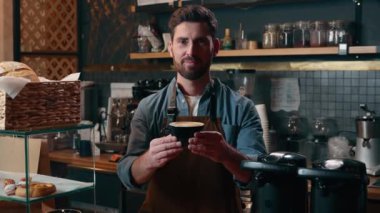 Beyaz tenli, küçük işletme sahibi, barista çalışanı, elinde bir fincan lezzetli kahve, gülümseyen adam garsonlar, kafeteryadaki barmen erkek, kapuçino, latte müşterisine kahve ikram ediyor.