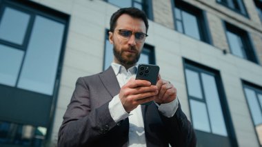 Düşünceli iş adamı, yetişkin, açık havada şüpheli beyaz adam akıllı telefon uygulaması e-ticaret online sohbet ile çalışan cep telefonu işveren erkek girişimci CEO 'su kullanıyor.