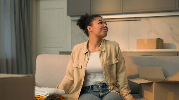 Афро-американская этническая женщина счастливая девушка домовладелица арендатор распаковывает коробку на диване, переезжая в новый дом веселый улыбающийся женщина клиент распаковать посылку заказ одежды онлайн доставки товаров день