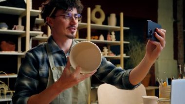 Gülümseyen erkek blog yazarı, çömlekçi, heykeltıraş, sosyal medya, blog, cep telefonu, el sanatları, kase, sanat atölyesi, beyaz adam, seramik dükkanında küçük işletme sahibi.