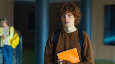 Lise gençlik eğitimi. Koridorda tek başına kitap tutarken sakin ol. Kafkasyalı erkek öğrenci.