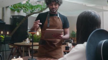 Gülümseyen Hintli Arap adam, kafeterya çalışanı, kafeterya şefi, müşteri hizmetleri müşterisi, restoran dijital tabletinde yemek siparişi veriyor, kahve dükkanında ziyaretçilere servis yapıyor.