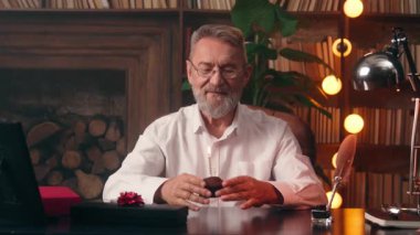 Mutlu, neşeli, yaşlı, beyaz adam mum pastası üflüyor. Doğum günü tatili. Yaşlı emekli, olgun erkek yuvasını kutluyor.