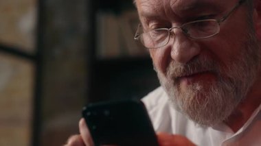 Kafkasyalı bir adam cep telefonu kullanıyor, akıllı telefon kullanıyor, internetten sohbet ediyor, mesajlaşıyor, mutlu, yaşlı, yaşlı, gülümseyen iş adamları, ev içi web gözlükleri takıyor.