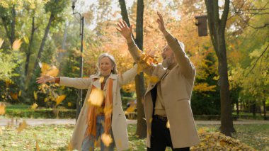 Emekli çift, çılgın, mutlu erkek, dışarıda birlikte eğleniyor. İki büyük anne ve büyük baba, yaşlı eş, koca, kadın, sonbahar parkında sarı yapraklar fırlatıp sonbahar doğası şehrinin tadını çıkarıyor.