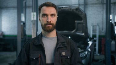 Kafkasyalı yetişkin erkek portresi. Ciddi bir makine mühendisi, teknisyen, elektrikçi, otomobil servisi kameralarına bakan endüstriyel tamirci.